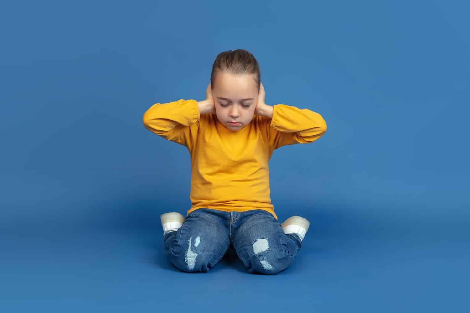 portrait of sad little girl sitting isolated on blue studio background how it feels to be autist modern problems new vision of social issues concept of autism childhood healthcare medicine