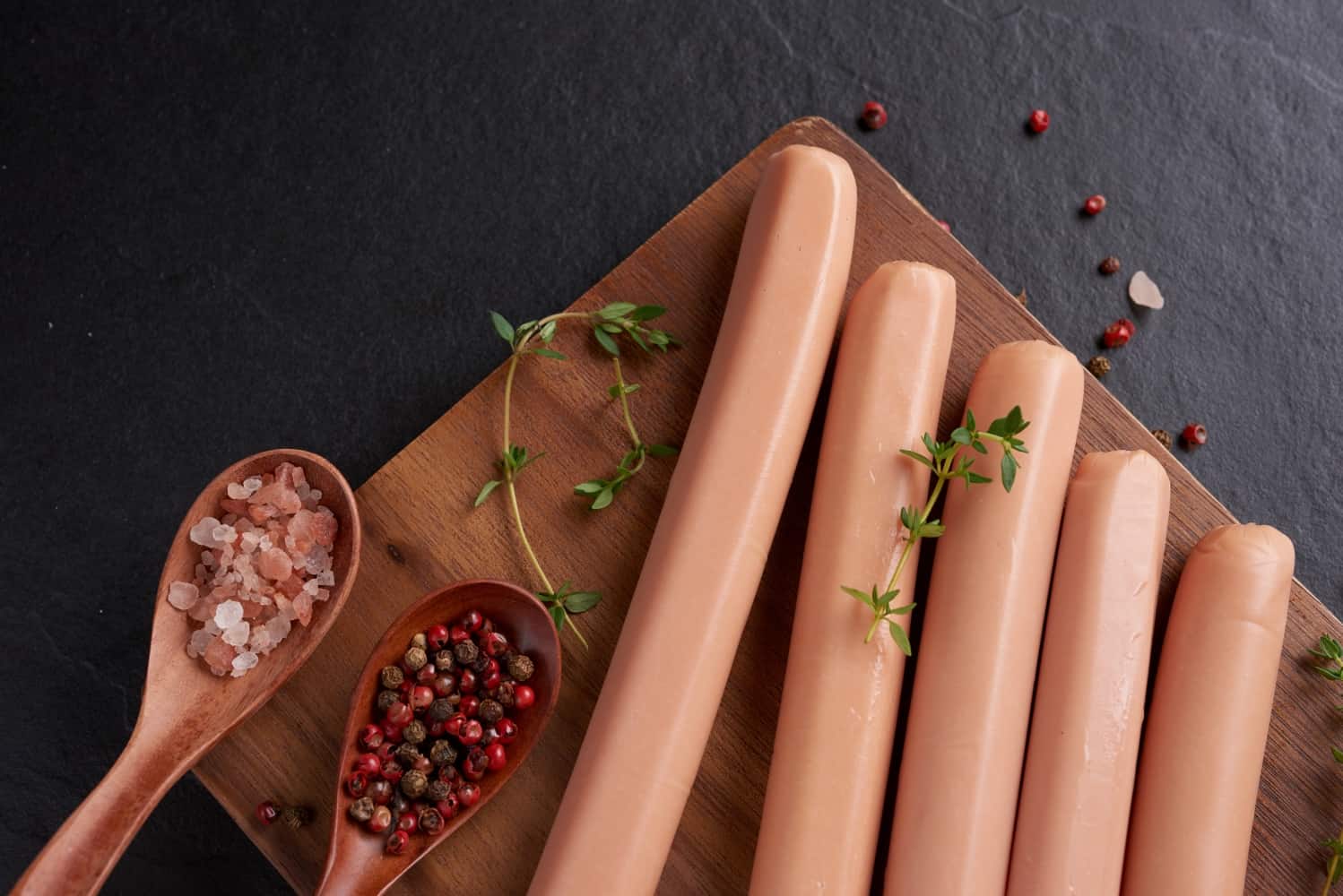 classic boiled meat pork sausages chopping board with pepper basil parsley thyme cherry tomatoes snack kid black surface sausages with spices herbs selective focus