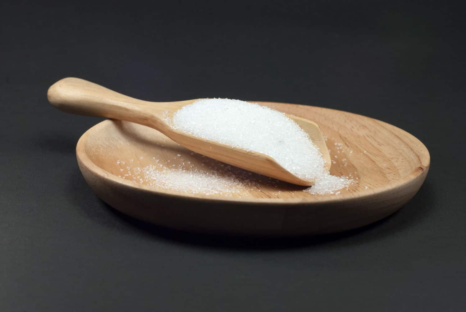 Qual a quantidade diária de sal e sódio que devemos consumir? 1 sugar wooden spoon placed wooden plate black background